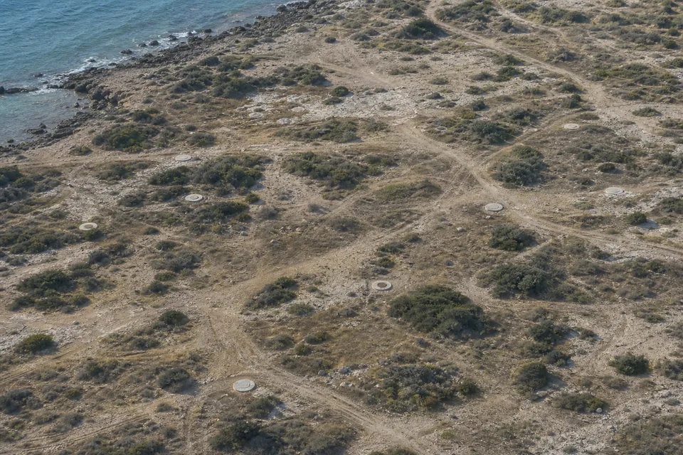 An ambiguous aerial view of similar utility covers, rocks, scrub and tracks across coastal terrain.